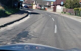 Opotrebovaná vozovka cesty II/501 s rozpadnutým okrajom a záplatami pri chodníku v obci Cerová pred rekonštrukciou