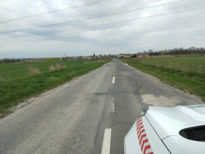 Poškodená cesta III/1130 so záplatami a výtlkmi medzi poliami, v pozadí Skalica, pred rekonštrukciou úseku k hranici
