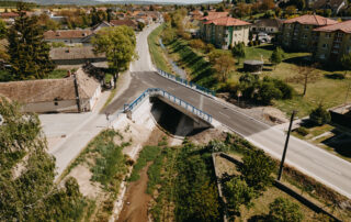 Zrekonštruovaný most na ceste v obci, letecký pohľad na novú vozovku, zábradlie a upravené koryto potoka